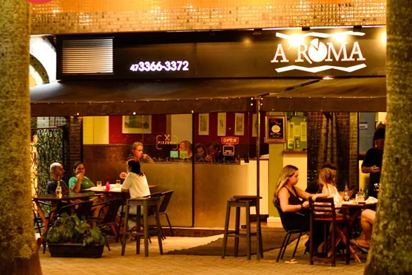Fachada do restaurante Aroma à noite, com clientes sentados nas mesas ao ar livre, desfrutando do ambiente acolhedor.