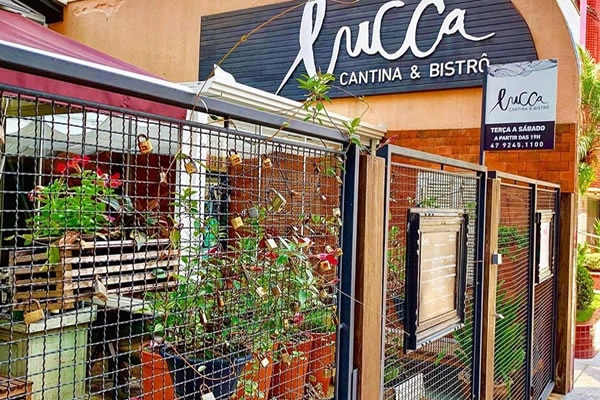 Fachada do Lucca Cantina & Bistrô, decorada com plantas e uma estrutura de arame, com o letreiro visível acima da entrada.