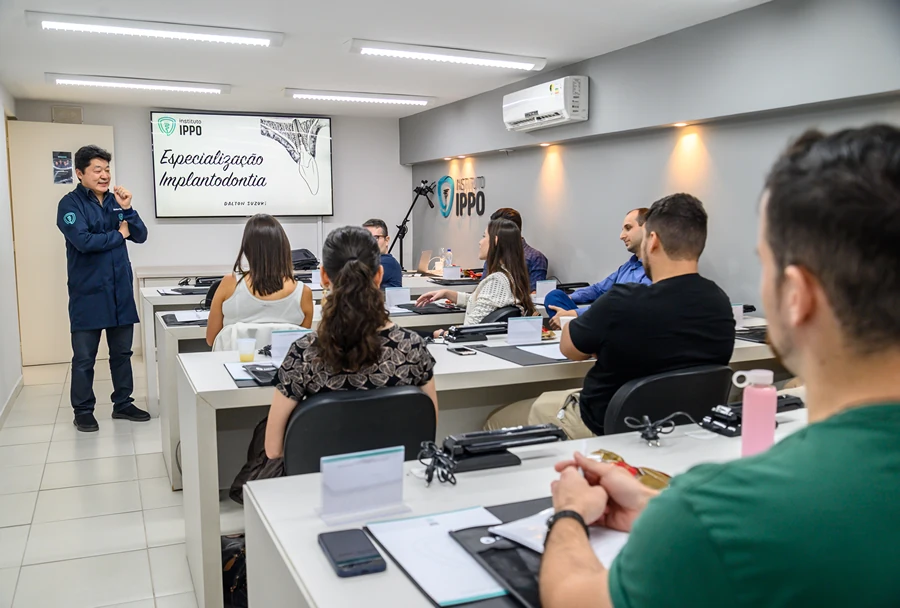 Professor Dalton Suzuki no Instituto IPPO, em frente a uma apresentação sobre "Especialização em Implantodontia", interagindo com os alunos que assistem atentamente.