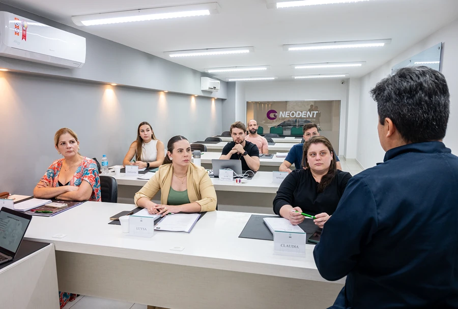 Turma de alunos do Instituto IPPO ouvindo atentamente o instrutor em uma aula sobre Implantodontia, com a marca Neodent visível no fundo.