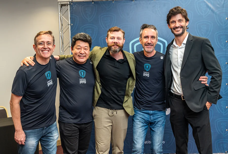 Cinco homens sorridentes do IPPO, quatro em camisetas azuis com logo, um em terno preto, posando juntos, fundo azul com símbolo IPPO.