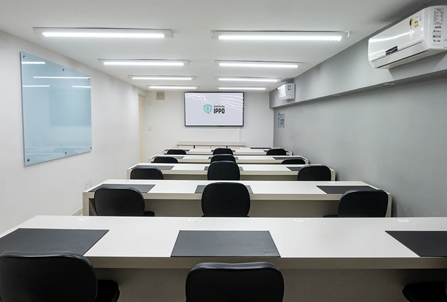 Sala de aula no Instituto IPPO, com mesas e cadeiras organizadas para uma apresentação, e uma tela de projeção com o logotipo do IPPO.