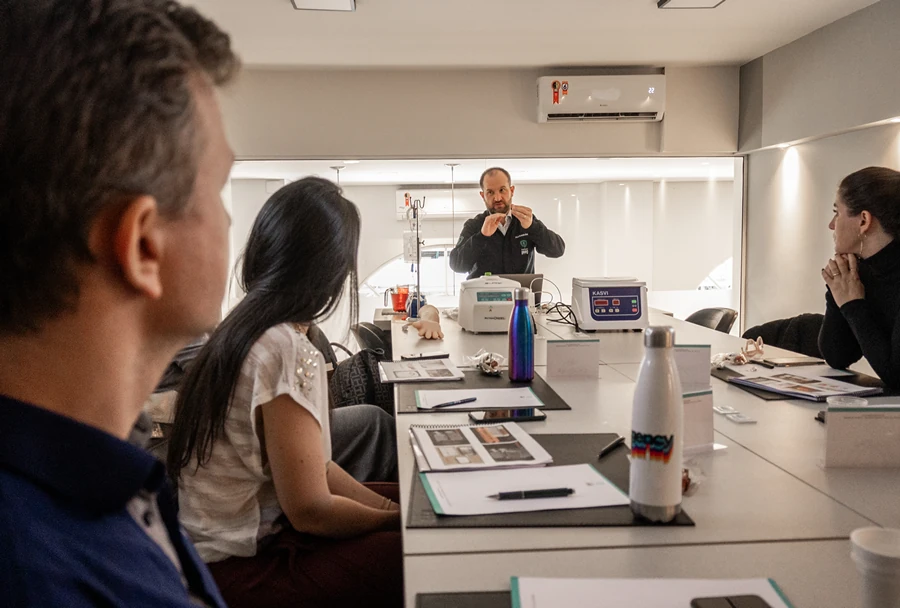 Instrutor do Instituto IPPO realizando uma explicação prática para os alunos, com materiais de aprendizado dispostos sobre a mesa.