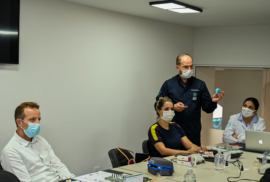 Instrutor do Instituto IPPO usando um modelo de dente para demonstrar uma técnica, com participantes assistindo atentamente.